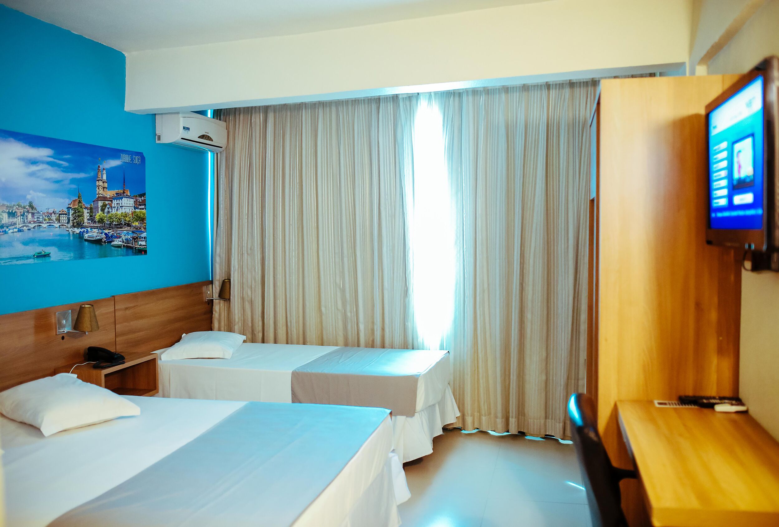 Habitación de hotel con dos camas, un televisor y un cuadro de un paisaje urbano.