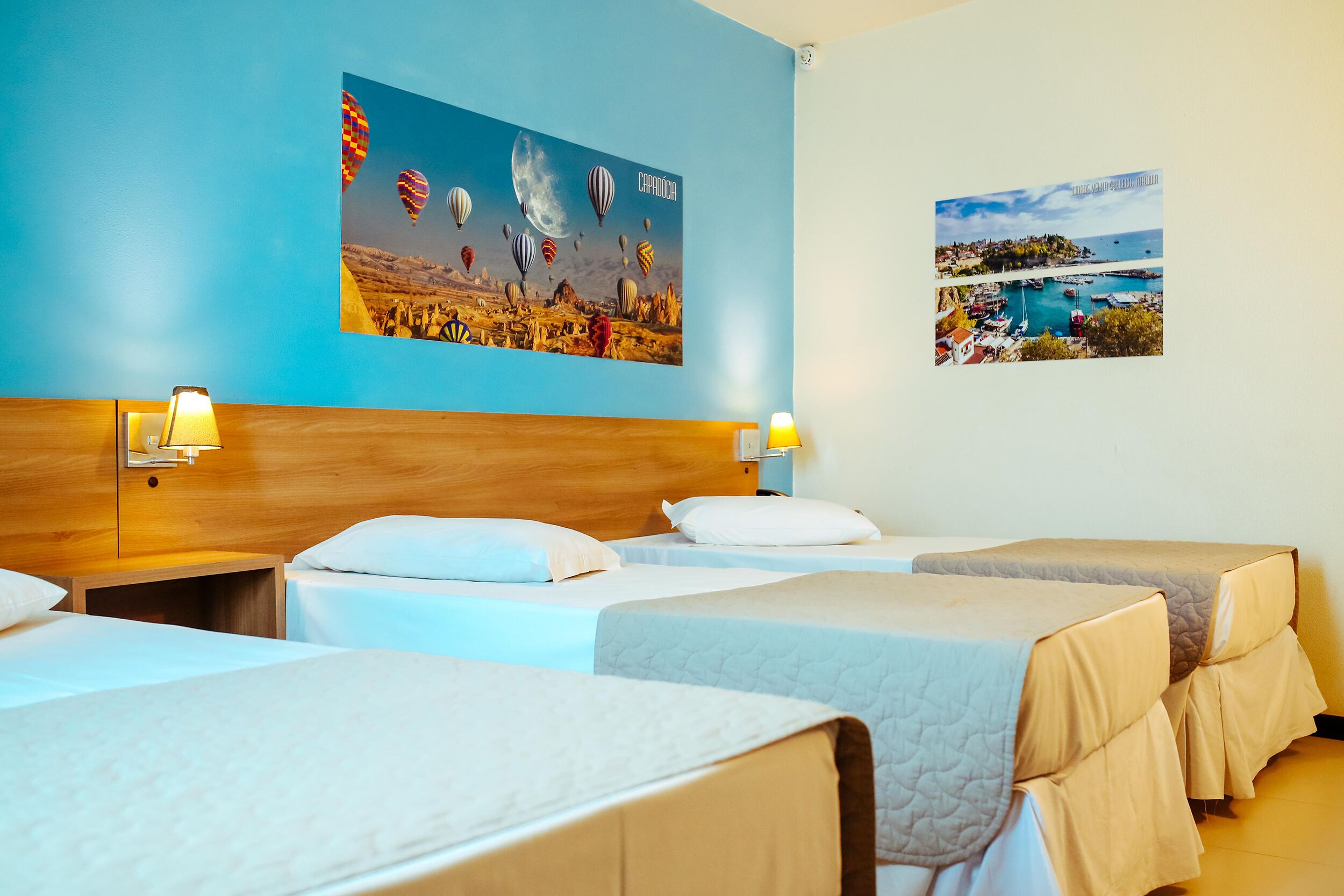 A hotel room with three beds, a wooden headboard, and two wall-mounted lamps.