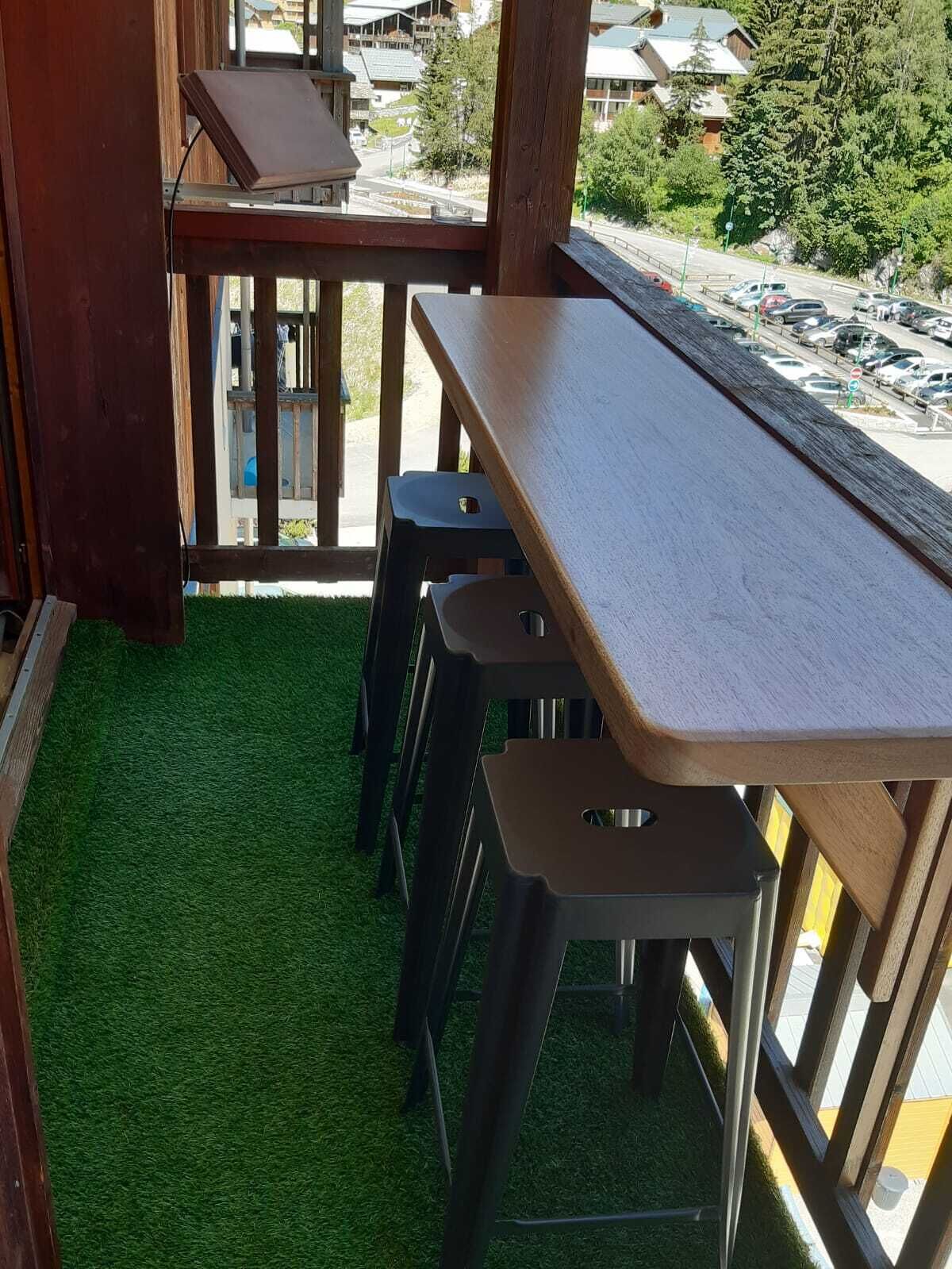 Eine Holzterrasse mit einem langen Tisch und vier Hockern, umgeben von einem grünen Kunstrasenteppich.