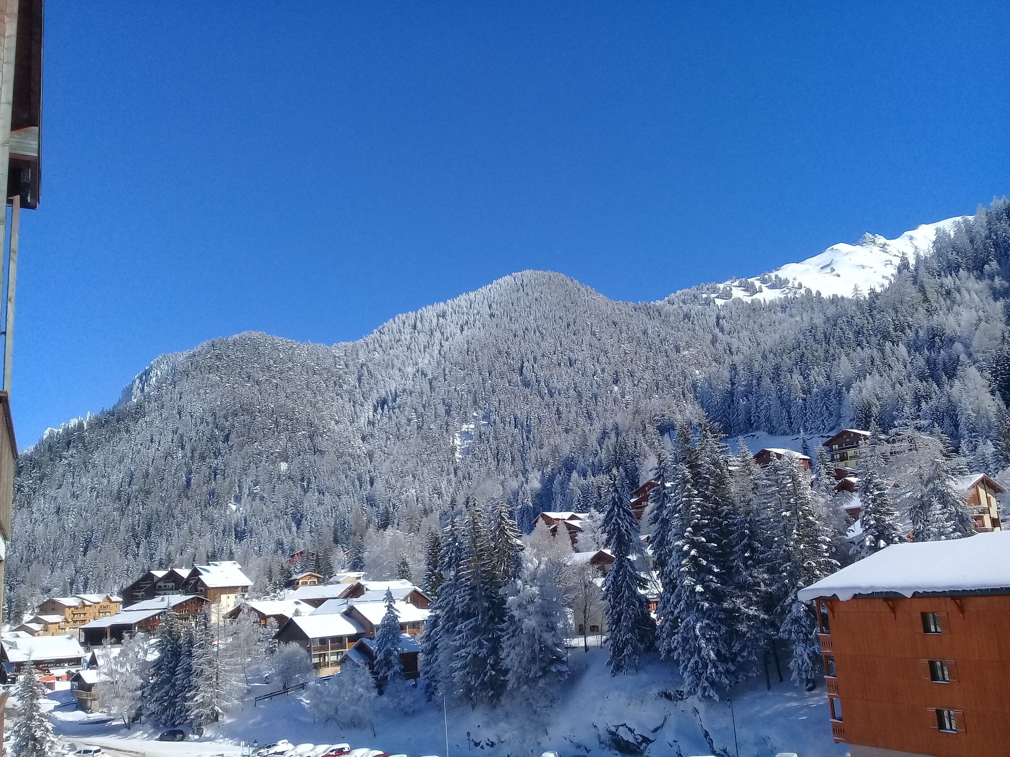 A snow-covered mountain with a ski resort in the foreground, featuring wooden buildings and snow-laden trees.