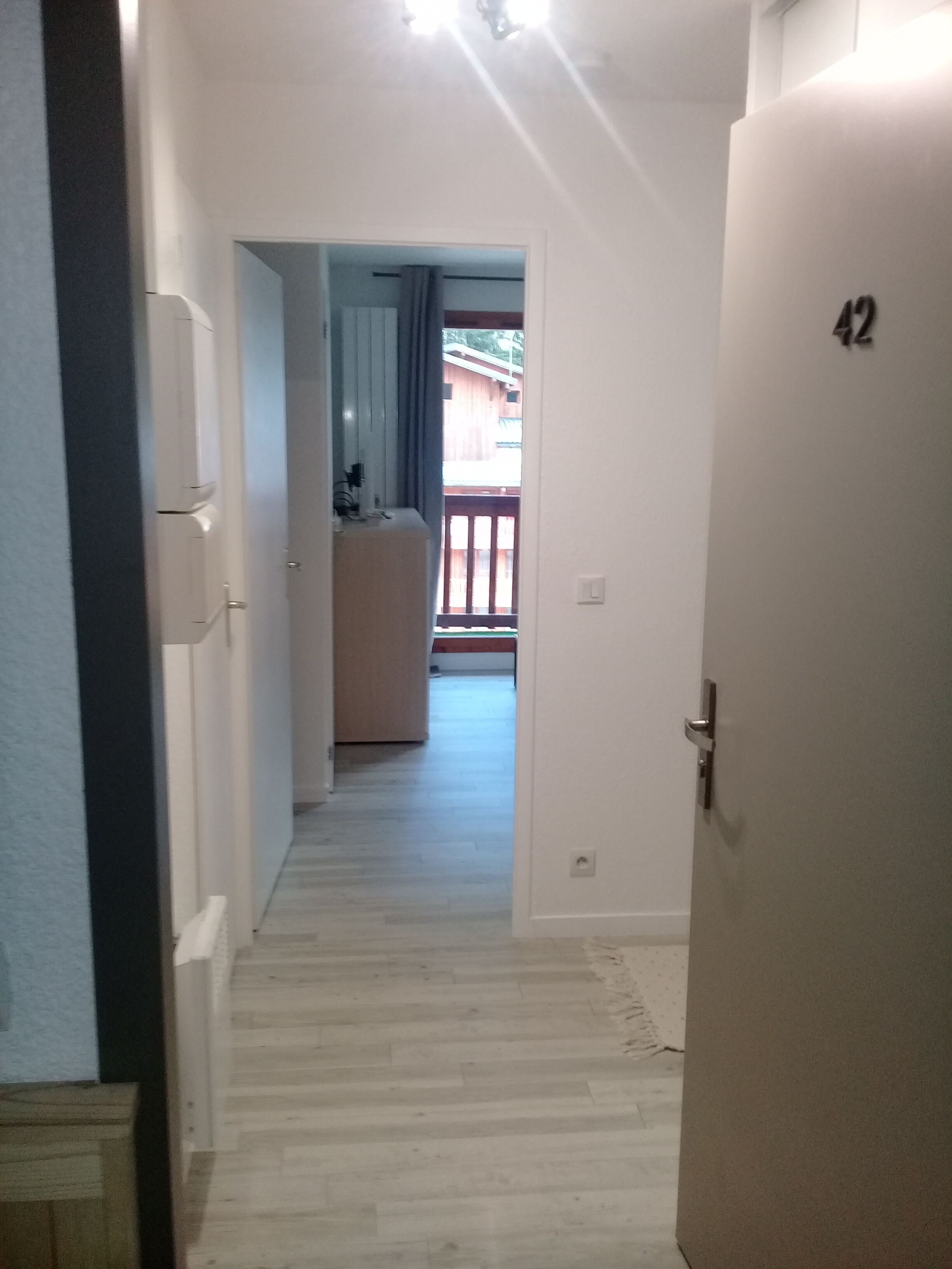 Ein Flur mit Holzboden, der zu einem Zimmer mit Balkon führt.