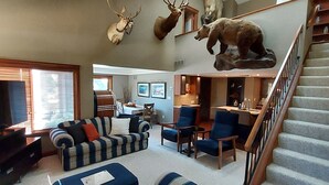 Ein Wohnzimmer mit Fernseher, Sofa und Sesseln. An den Wänden befinden sich aufgehängte Tierköpfe.