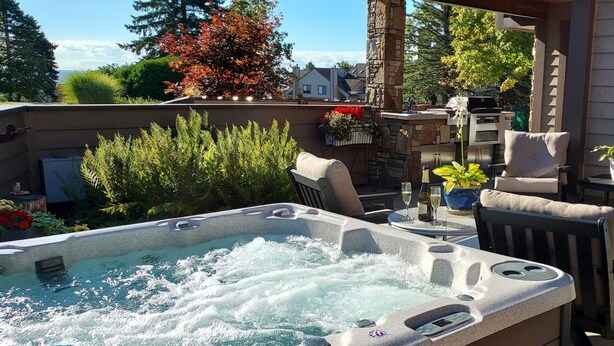 Ein Whirlpool mit Sitzgelegenheiten und Grill, umgeben von Topfpflanzen und Gartenmöbeln.