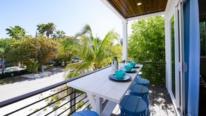 A covered outdoor dining area with a white table and blue chairs, surrounded by lush greenery and palm trees.