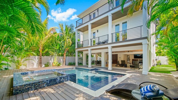 A modern two-story house with a swimming pool, outdoor furniture, and lush greenery.