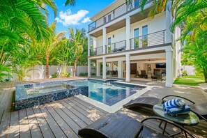 A modern two-story house with a swimming pool, outdoor furniture, and lush greenery.