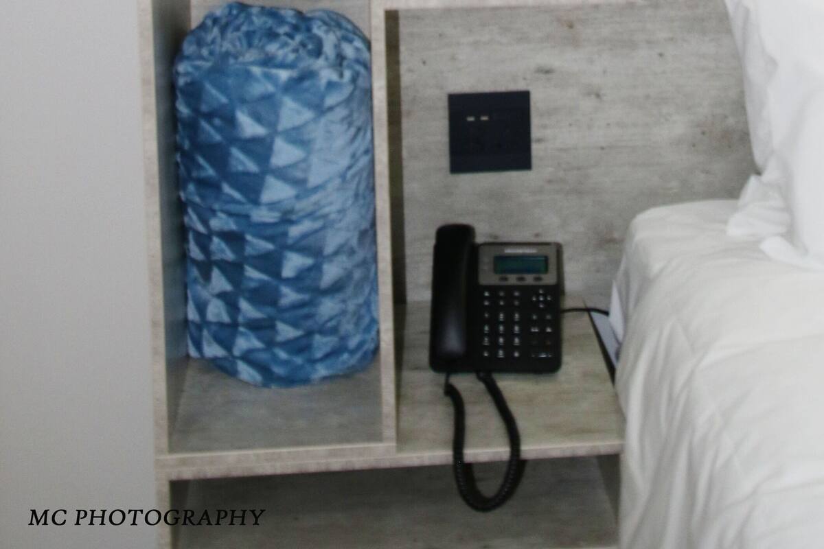A room with a built-in wardrobe, a blue patterned bag, a black telephone, and a white bed.