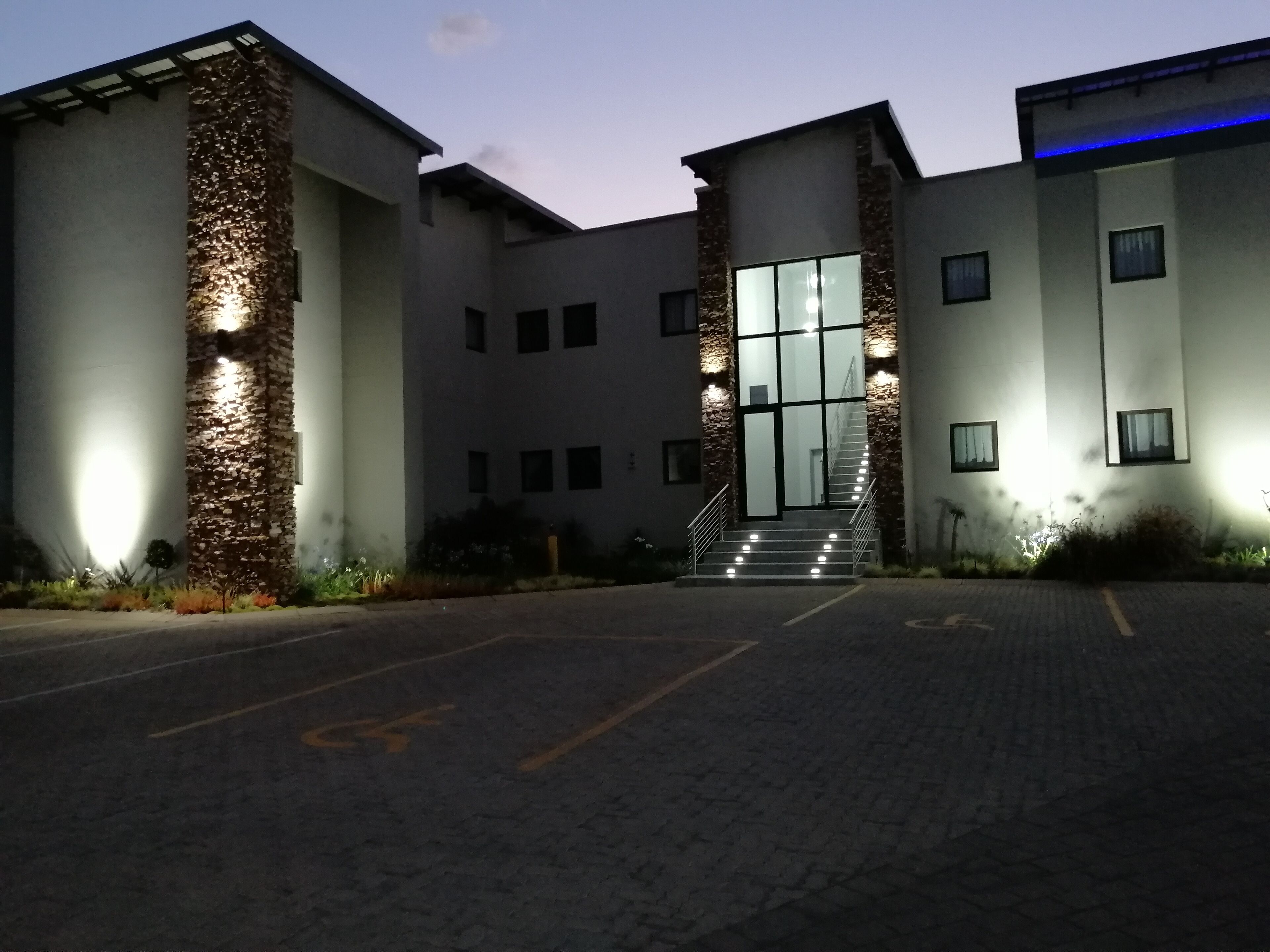 A building with a central staircase, a parking area, and a stone facade.