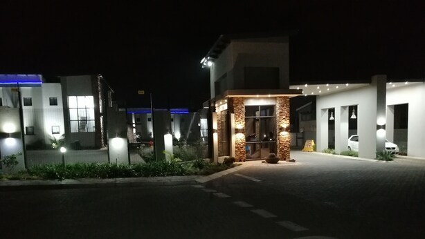 A well-lit hotel entrance with a stone facade, a clear pathway, and a parking area.