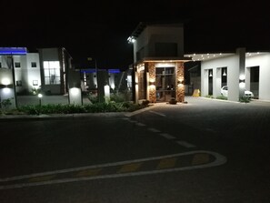 A well-lit hotel entrance with a stone facade, a clear pathway, and a parking area.
