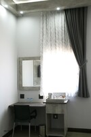 Una habitación pequeña y moderna con escritorio, silla y un ventanal con cortinas.