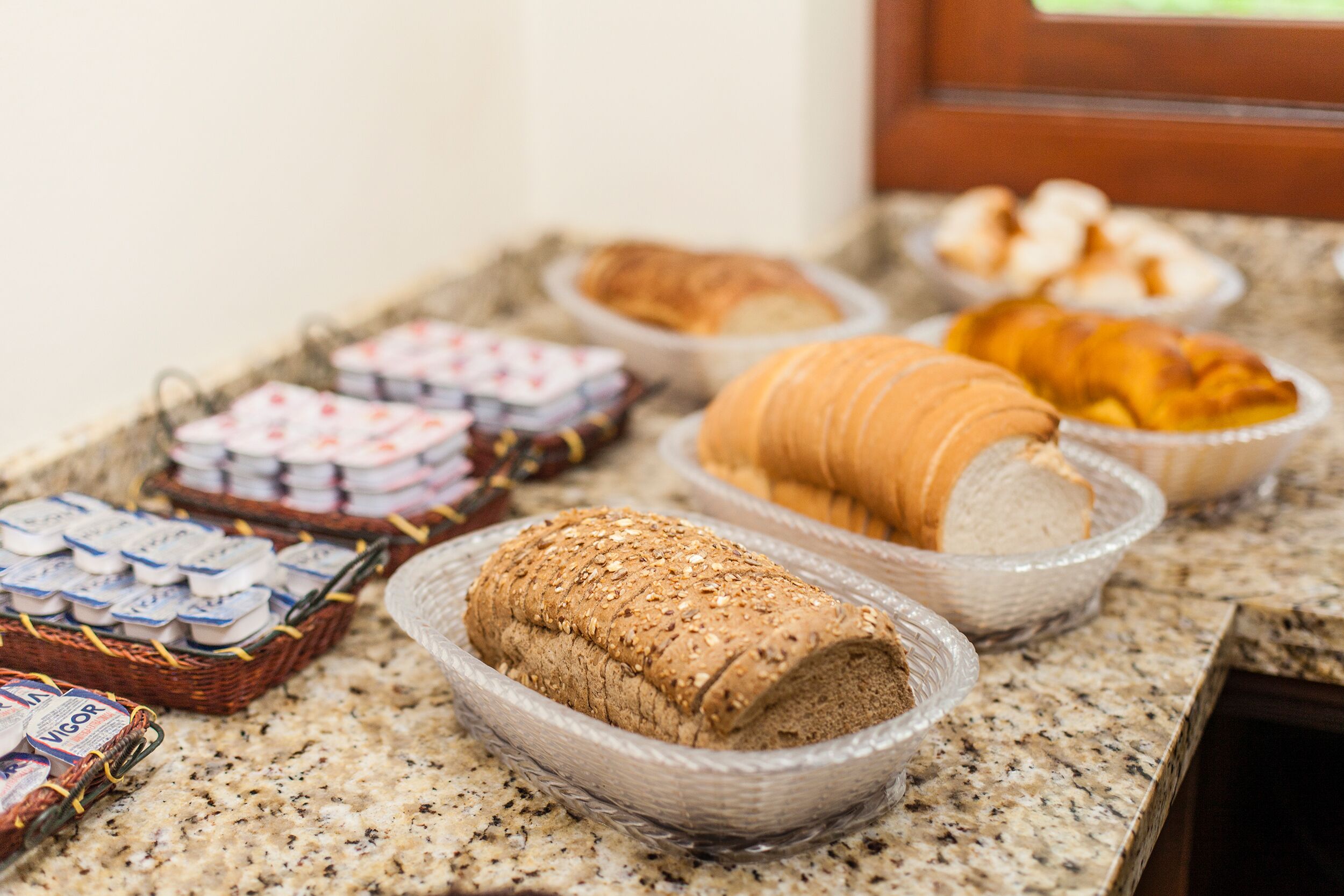 A buffet table with various breads and pastries, including a loaf of whole grain bread and croissants.