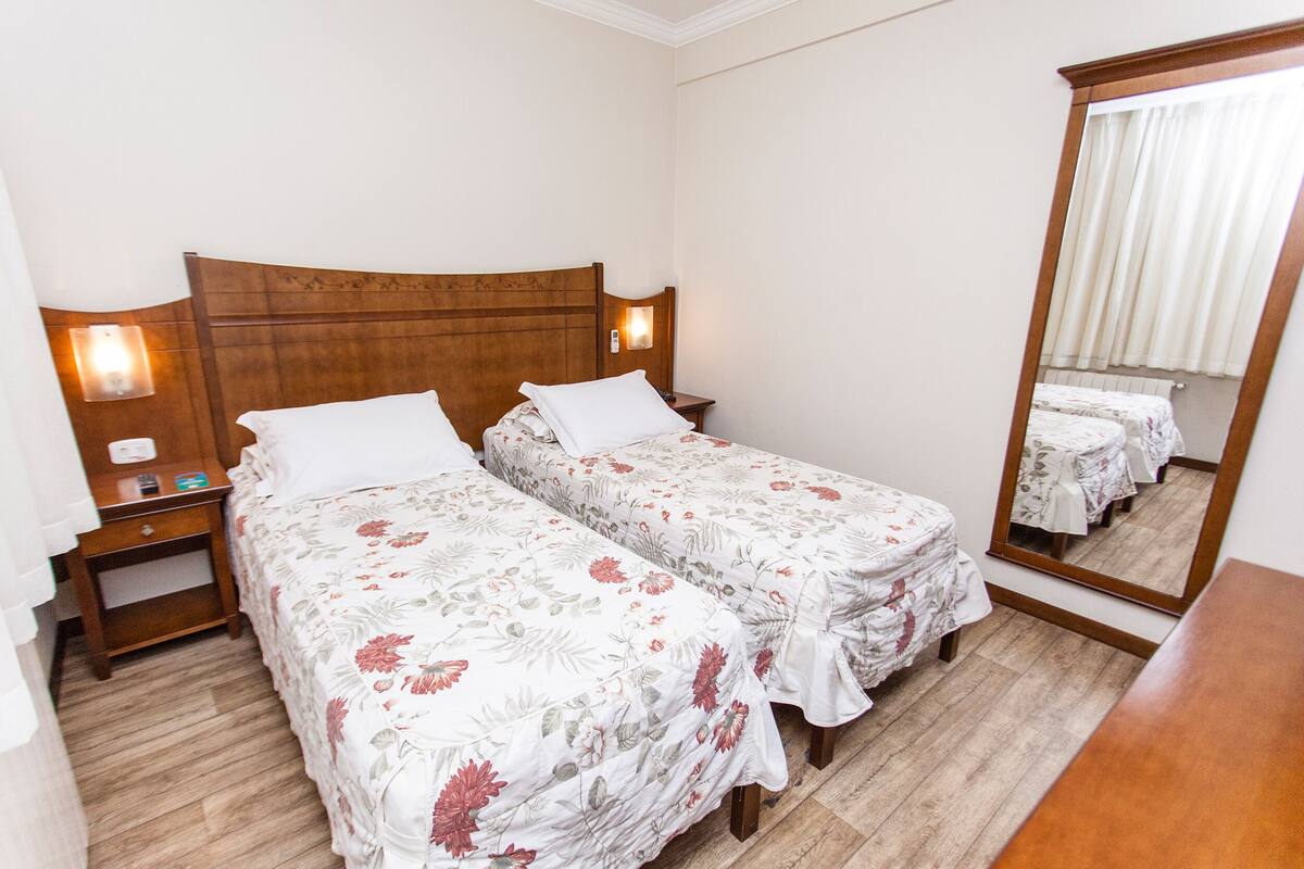 A hotel room with two single beds, wooden headboards, bedside tables, and a mirror.