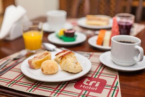 A breakfast setting with croissants, a glass of orange juice, and a cup of coffee on a table with a checkered placemat.