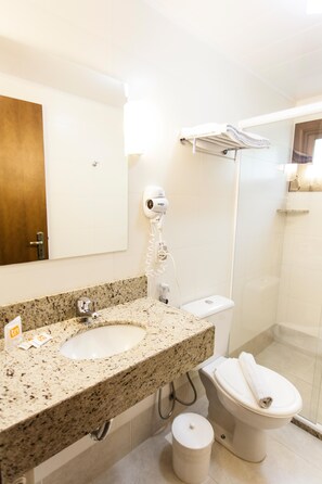 Un baño con lavamanos de encimera de granito, inodoro blanco, secador de pelo y cabina de ducha de vidrio.