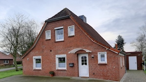 Une maison en briques rouges, avec un toit à pignon, une porte d’entrée et un petit porche.