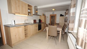 Une cuisine moderne avec des meubles en bois, un coin repas comprenant une table et des chaises, et une horloge visible au mur.