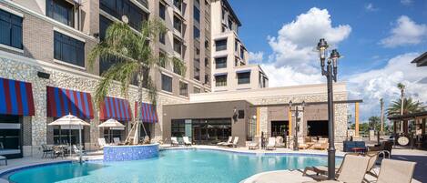A hotel with a swimming pool, outdoor seating, and a covered area with umbrellas.