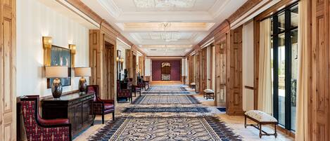 A long hallway with a patterned carpet, wooden paneling, and a chandelier.