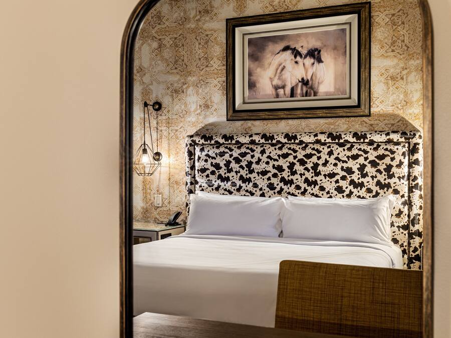 A hotel room with a bed, a nightstand, a lamp, and a framed picture on the wall.