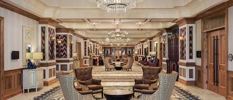 A spacious lobby with a grand chandelier, patterned carpets, and classic furniture.