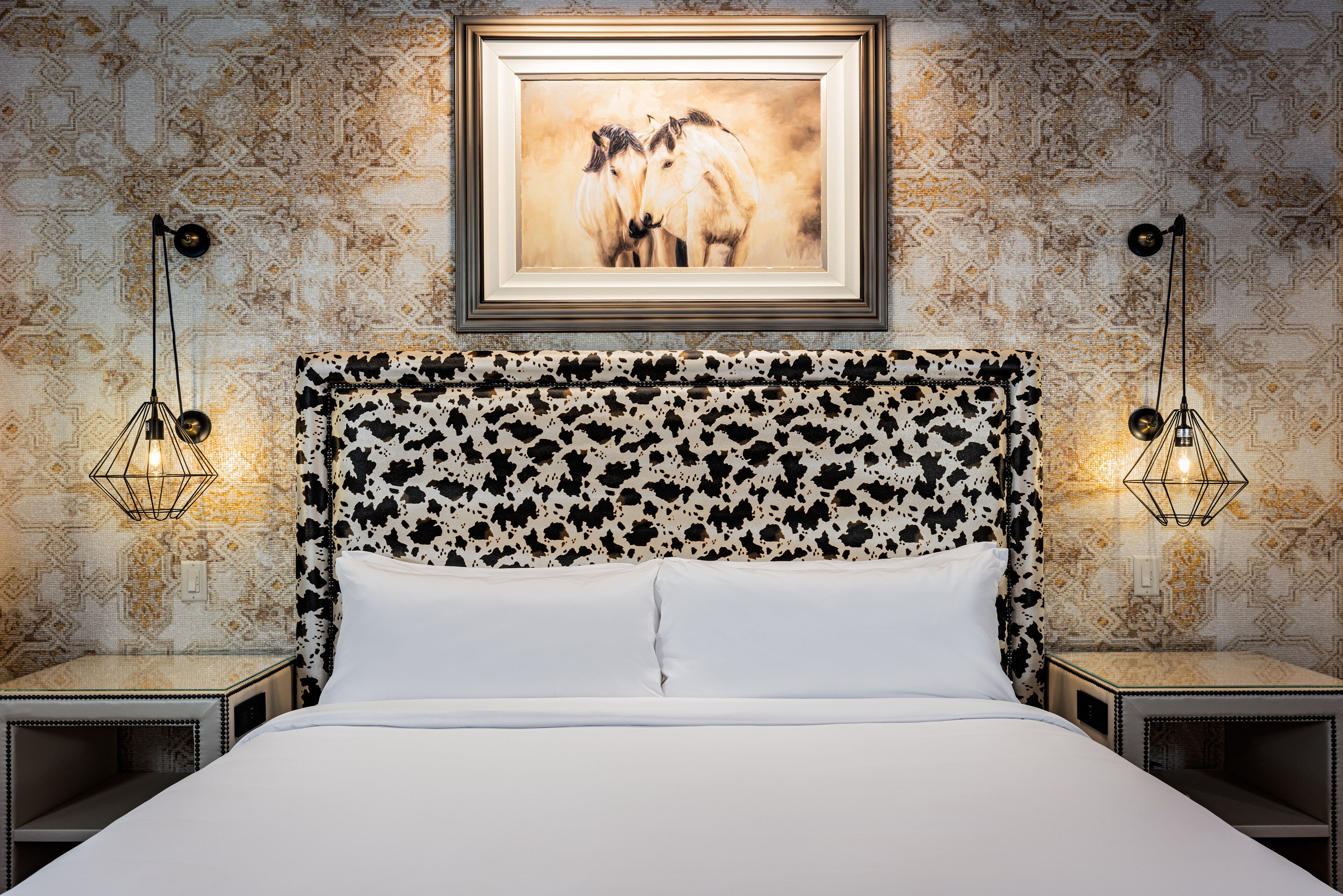 A bed with a patterned headboard, two bedside lamps, and a framed picture above the bed.