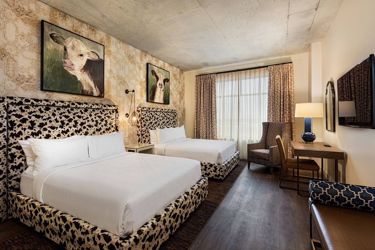 A hotel room with two beds, a desk, a chair, and a large window with curtains.