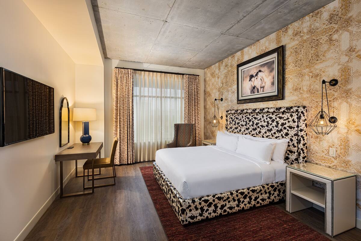 A hotel room with a bed, a desk, a chair, a lamp, and a picture on the wall.