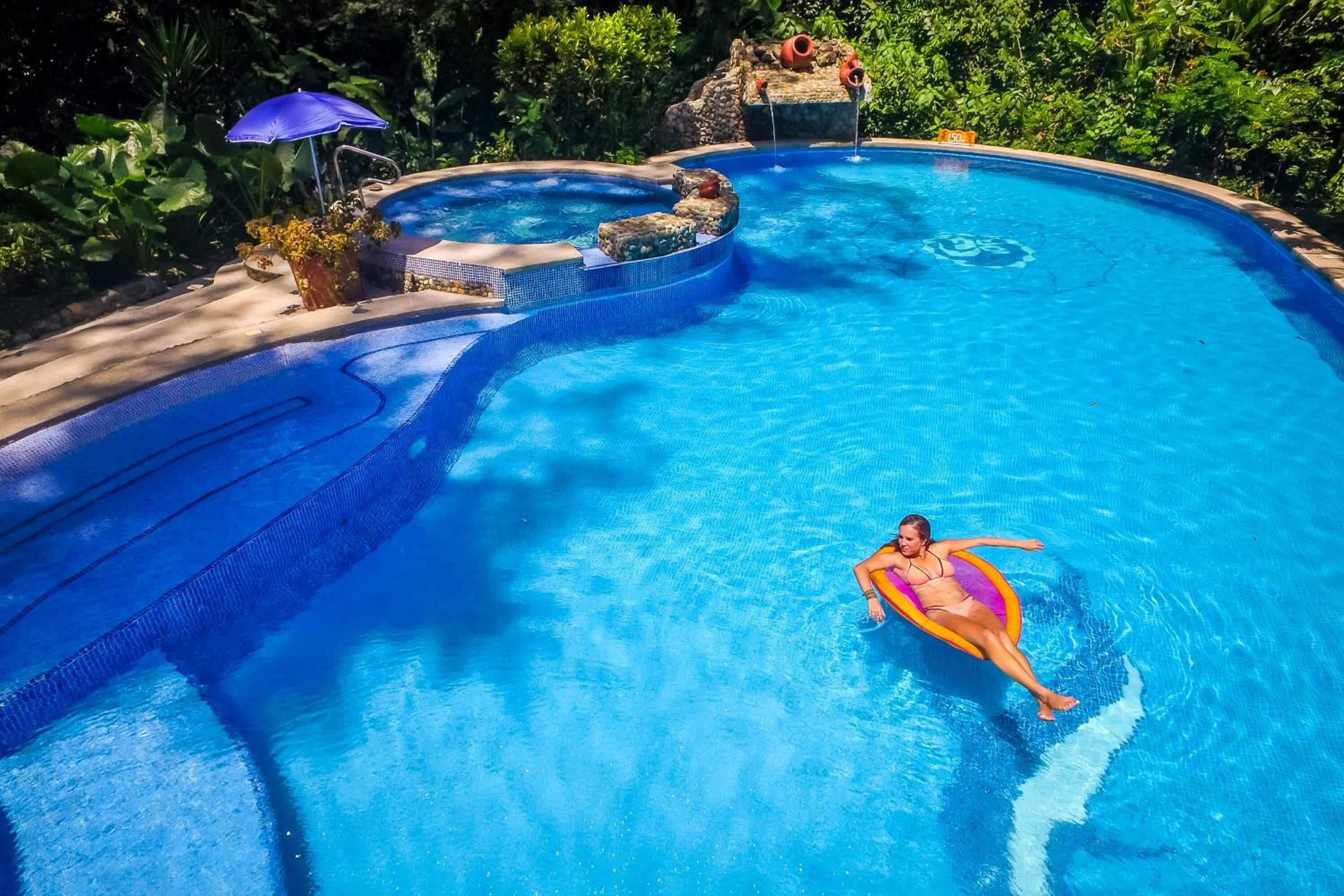 A swimming pool with a hot tub, surrounded by lush greenery.