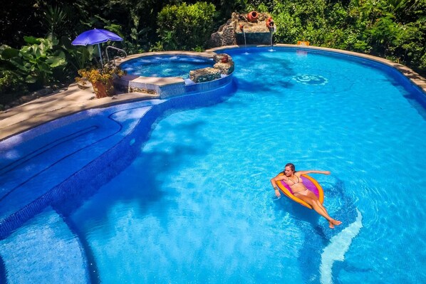 Una piscina con un jacuzzi, rodeada de abundante vegetación.