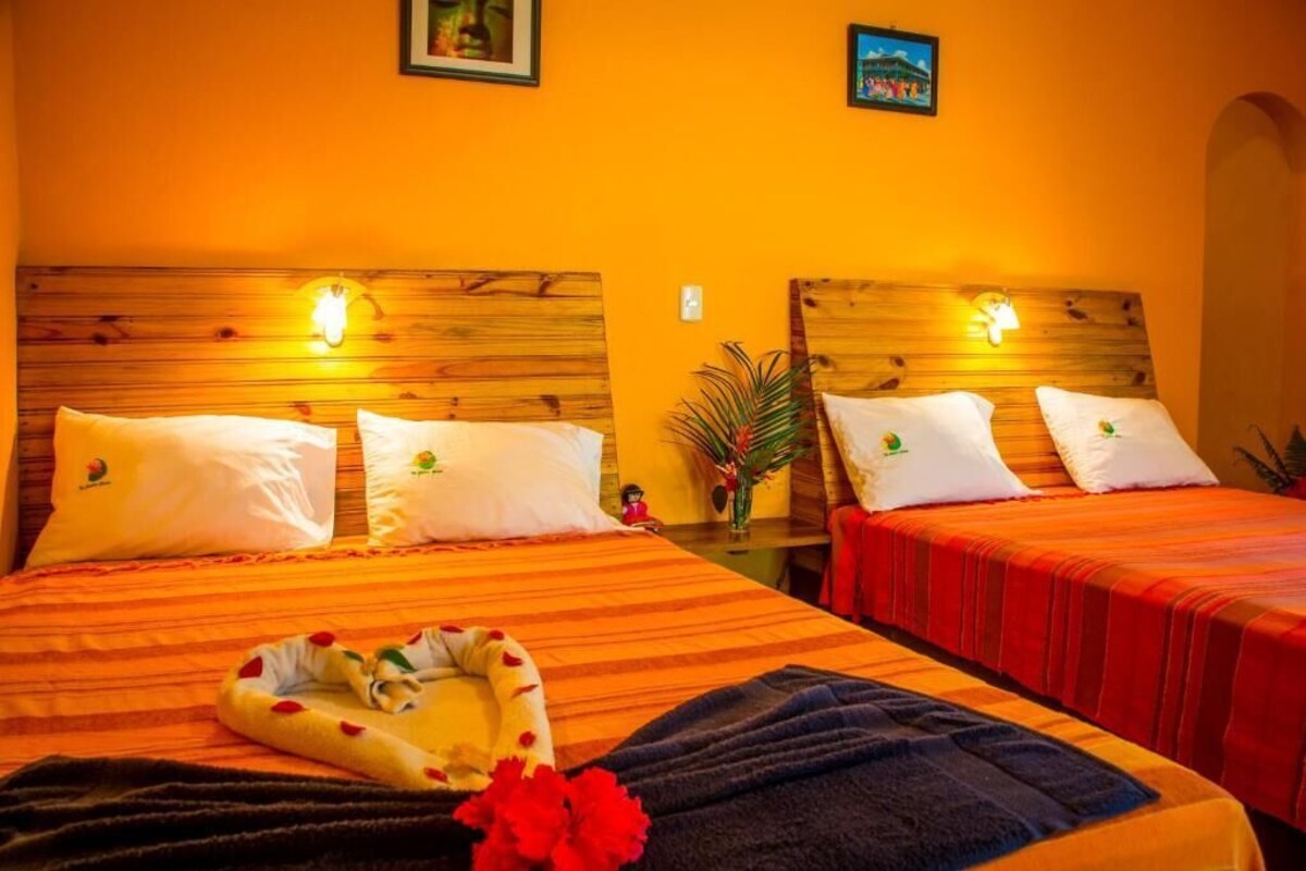 Une chambre d’hôtel avec deux lits, chacun doté d’une tête de lit en bois et d’oreillers blancs. On peut voir, sur le lit au premier plan, une composition florale en forme de cœur.