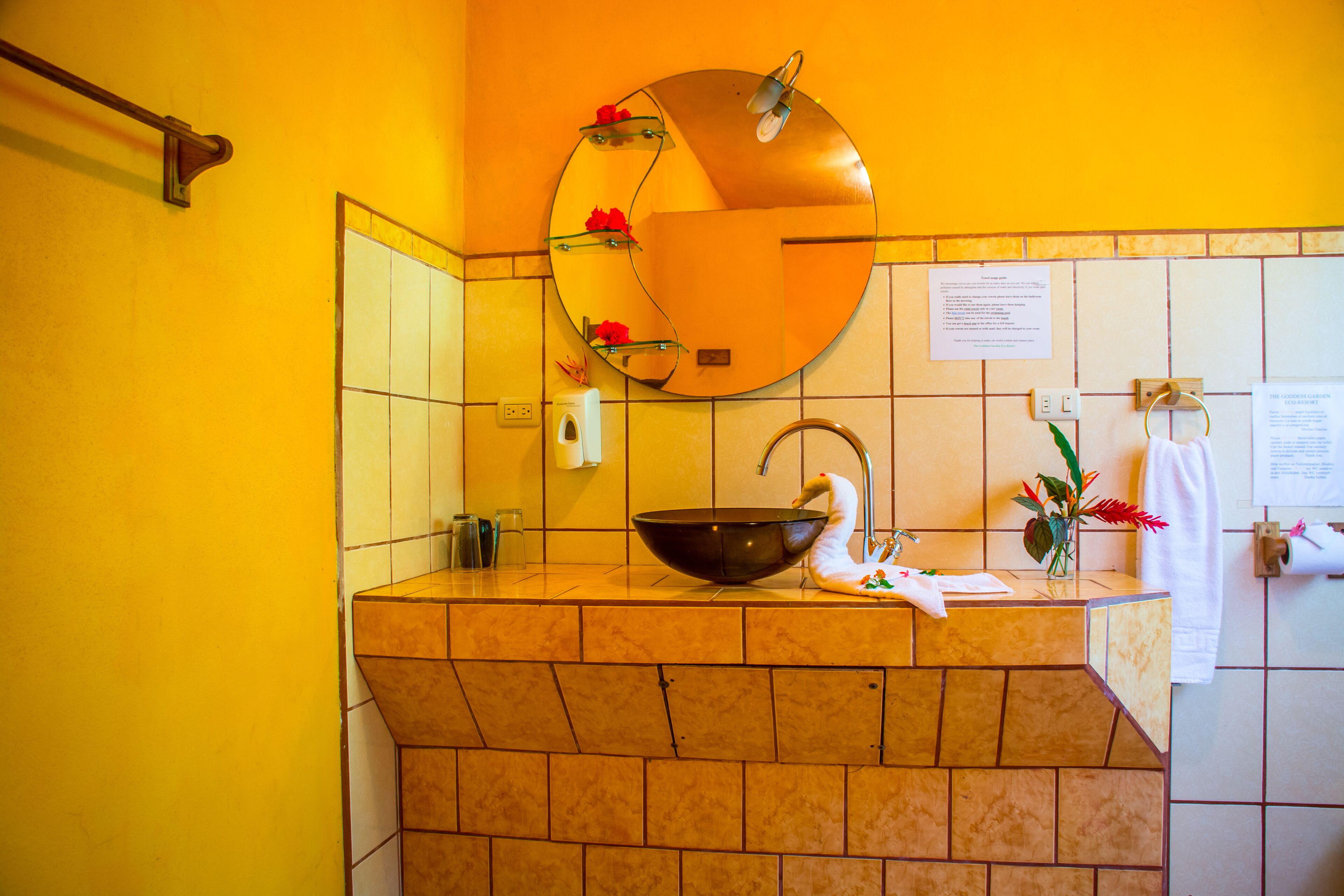 Une salle de bain avec un miroir rond, un lavabo noir en forme de bol et un porte-serviettes.