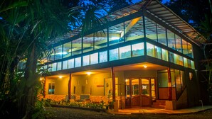 A modern building with a glass facade, a wooden deck, and a stone foundation. - The Goddess Garden (Cahuita)
