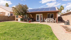 Una casa con paneles solares en el techo, un porche cubierto con mobiliario exterior y un césped bien cuidado.