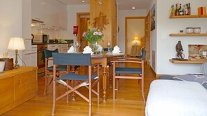 A modern living room with a dining area, wooden furniture, and a kitchen in the background.