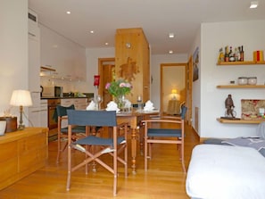 A modern living room with a dining area, wooden furniture, and a kitchen in the background.