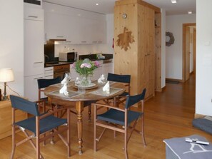 A dining area with a wooden table set for four, surrounded by chairs.