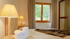 A hotel room with a bed, two bedside lamps, a window with curtains, and a view of greenery outside.