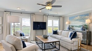 Una sala de estar con ventilador de techo, televisor de pantalla plana, sofá, mesa de centro y vistas al exterior.