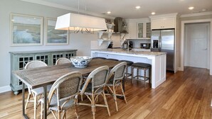Una cocina moderna con una isla central, armarios blancos y un comedor con sillas de mimbre.