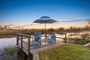Een houten terras met twee Adirondack-stoelen en een gestreept zonnescherm, met uitzicht op een rustig wateroppervlak.