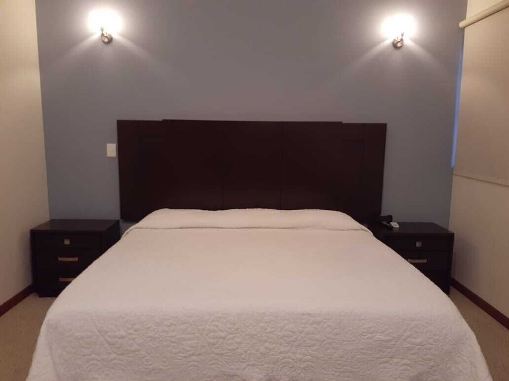 Una habitació d'hotel amb un llit gran, dues taules de nit i un panell de capçalera fosc.