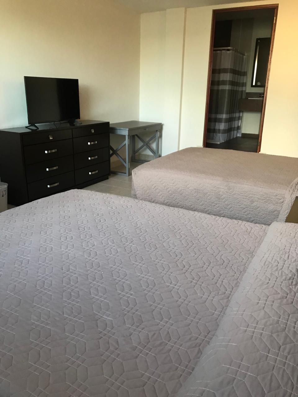 Une chambre avec deux lits, une commode, une télévision et une petite table.