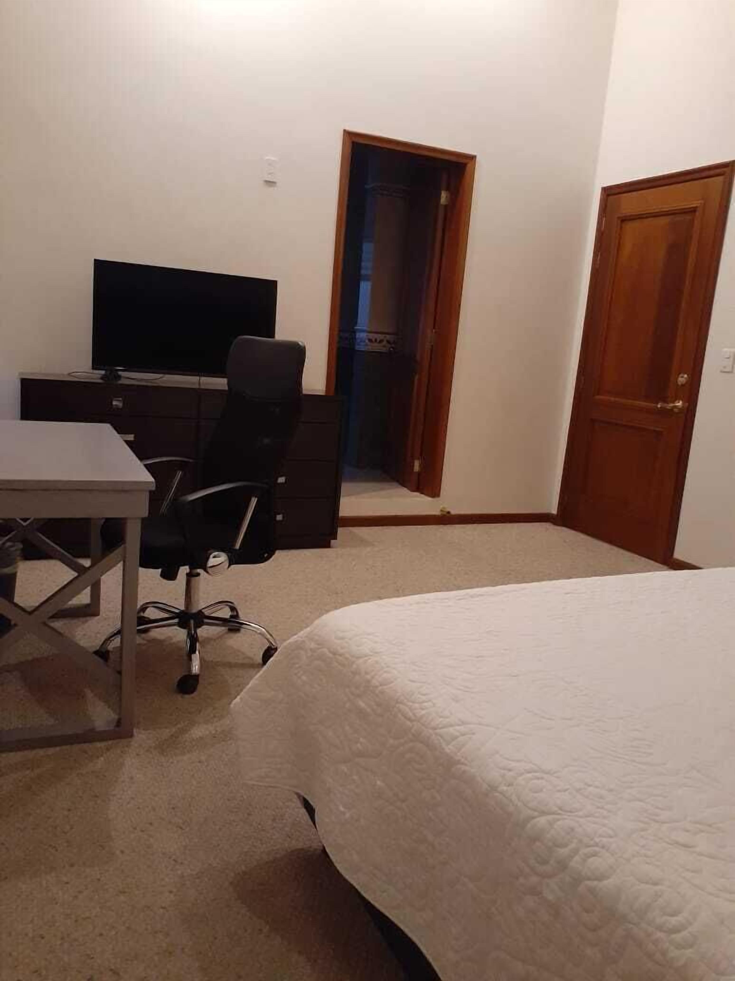 A bedroom with a bed, a desk, a chair, and a television.