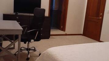 A bedroom with a bed, a desk, a chair, and a television.