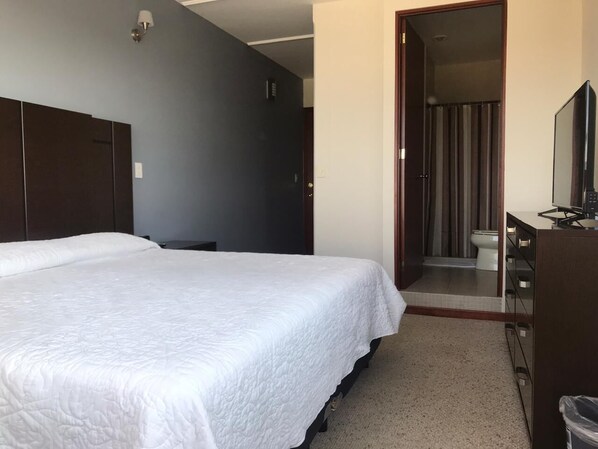 Un dormitorio con una cama grande, un aparador, un espejo y una puerta que da a un baño.