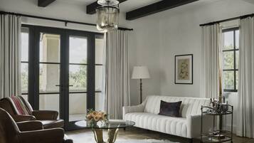 A modern living room with a white sofa, leather armchairs, a glass coffee table, and a metal side table.