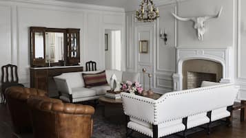 A traditional living room with a fireplace, leather armchair, white sofa, and a patterned rug.
