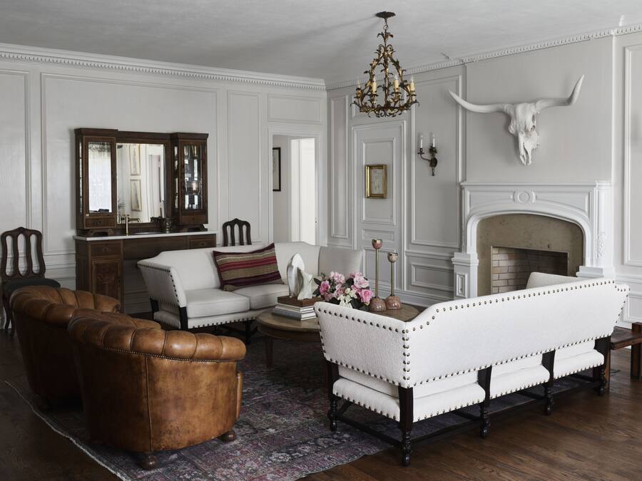 A traditional living room with a fireplace, leather armchair, white sofa, and a patterned rug.