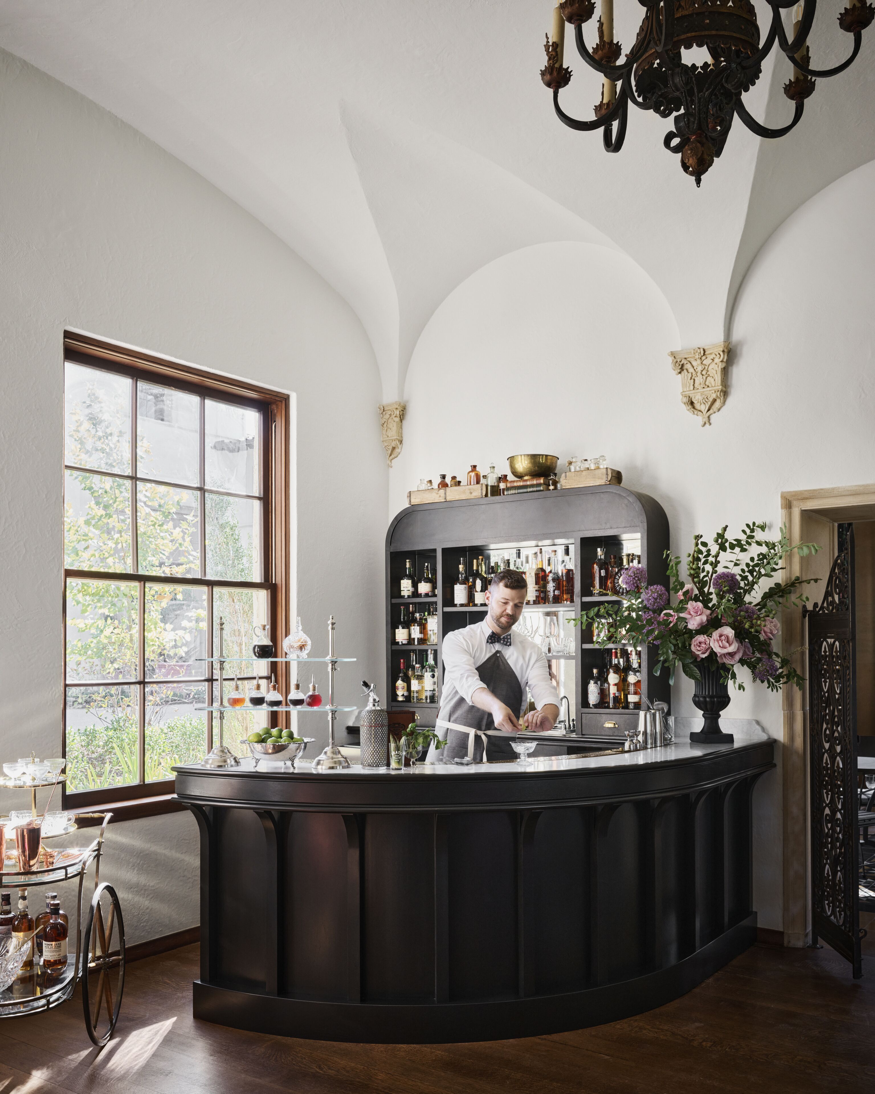 A bar area with a bartender, a large window, and shelves with bottles.
